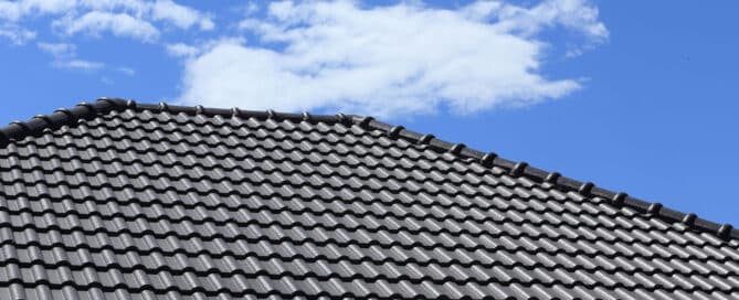 Close-up of gray tiled roof against a blue sky with clouds. "Common Roof Issues" visual.