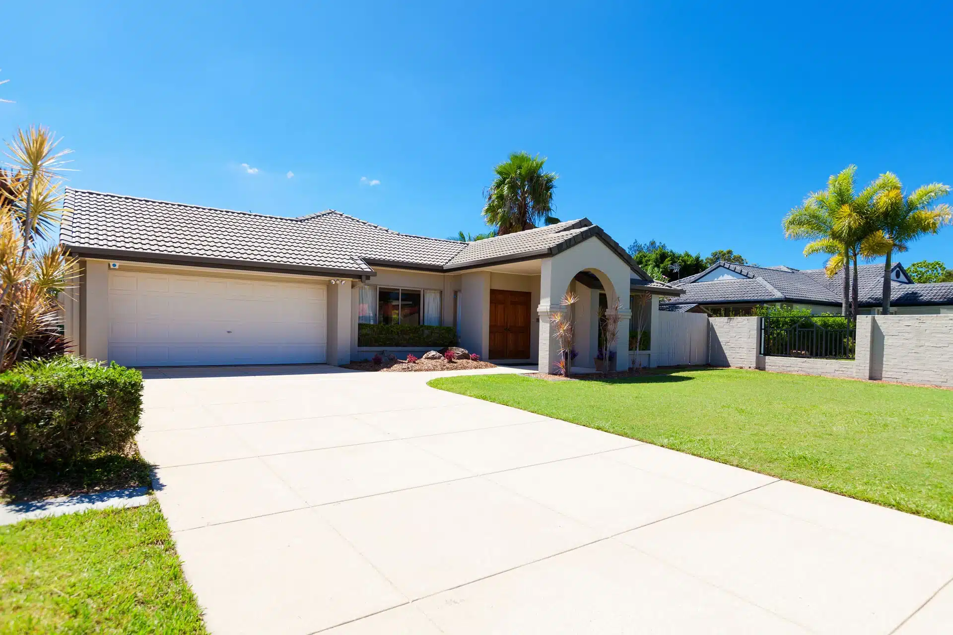 House with a "long-lasting roof". Tile roof on a modern home with manicured lawn and driveway under a bright blue sky.