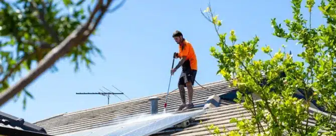 Solar panel cleaning. Technician pressure washing solar panels on a tiled roof, ensuring peak energy efficiency. "Permacoat"