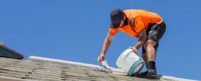 Roofer applying "Permacoat" roof sealant to tile roof. Worker in orange shirt with sealant bucket. Blue sky background.