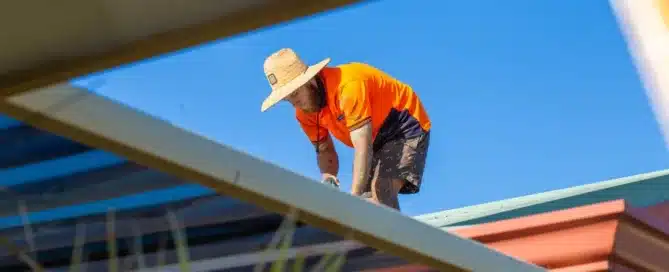 Permacoat" installer on roof. Worker in hat & hi-vis shirt. Blue sky background.