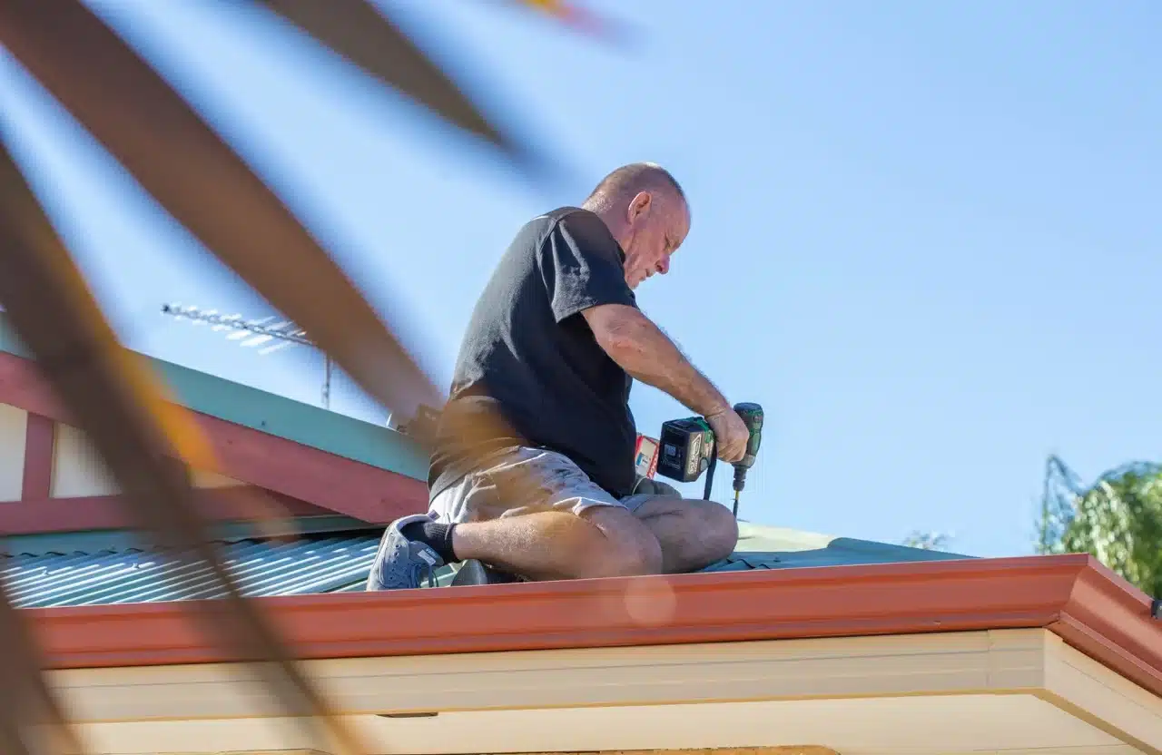 Man repairing roof with power drill. Shows "Permacoat" roofing expertise.