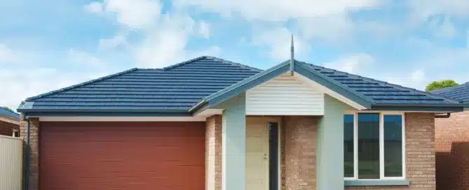 Dark grey roof tiles on a modern brick house with a brown garage door under a blue sky. "Roof Coating.