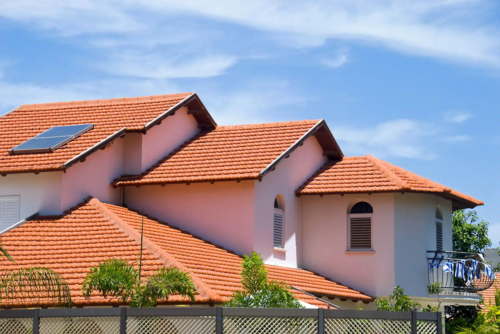 Orange tiled roof with a solar panel on a white house. "Roofing Safety" hazards.