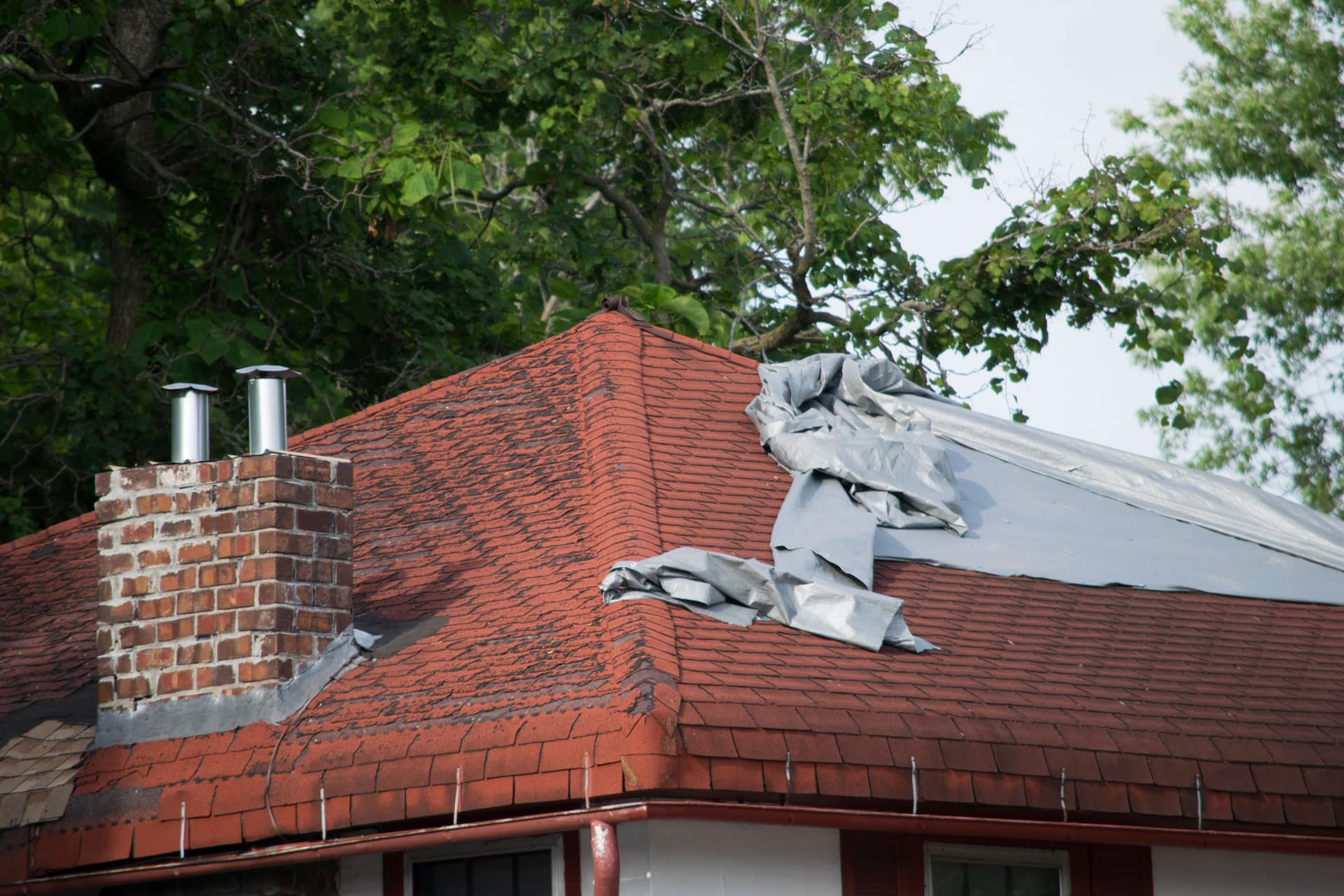 Damaged roof with missing shingles covered by a tarp. "Tell-Tale Signs that Your Roof Needs Repairing.