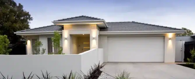 Modern single-story house with a white garage door, tiled roof, and rendered white front fence.